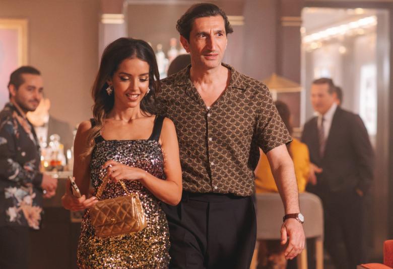 Kuvassa ovat etualalla oikealla ruskeassa paidassa ja mustissa housuissa Fares Fares. Hänen vieressään Lyna Khoudri kultakimalteisessa minimekossa. Taustalla on miehiä baaressa. 