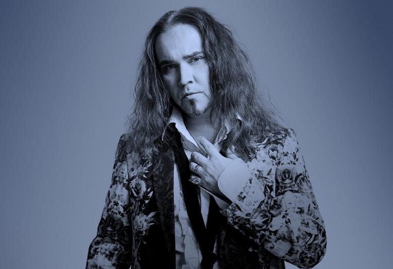 Kuvassa on Jarkko Ahola keskellä ja hänellä on kirjavasti kuvioitu takki päällään. Hänellä on pitkät, kiharat hiukset. Tausta ja kuvan sävy on sini-harmaa.