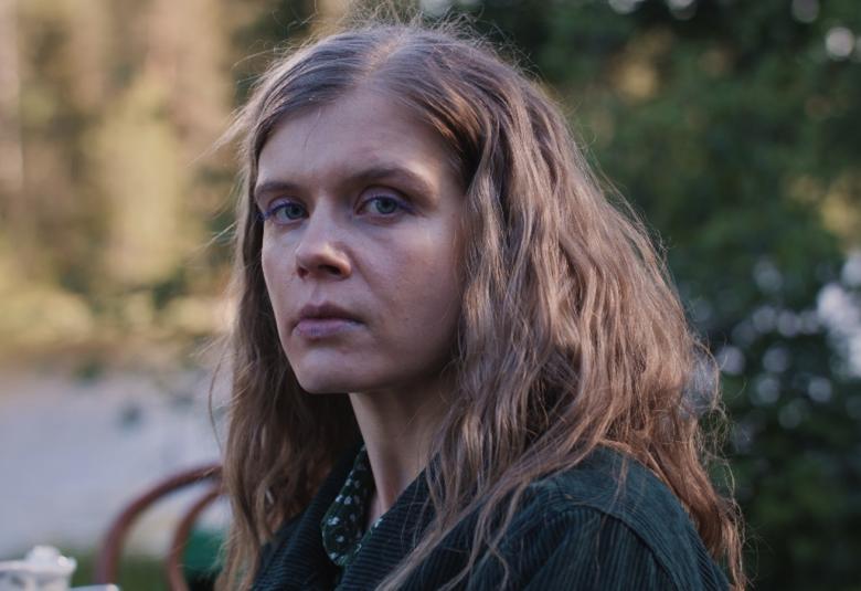 Kuvassa on Alina Tomnikov puolivartalokuvassa ja hänellä on pitkähköt ruskeat hiukset. Taustalla näkyy vihreää metsää.