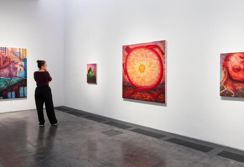 Kuvassa on vasemmassa kulmassa on sini-punertava teos ja pitkällä suoralla seinällä pieni taulu ja vieressä iso teos, jossa on iso keltainen ympärä sekä punainen kehä. Oikealla on pienempi teos, jossa on päälimmäisenä punainen pallo. Teoksia katsoo vasemmalla nuori nainen.