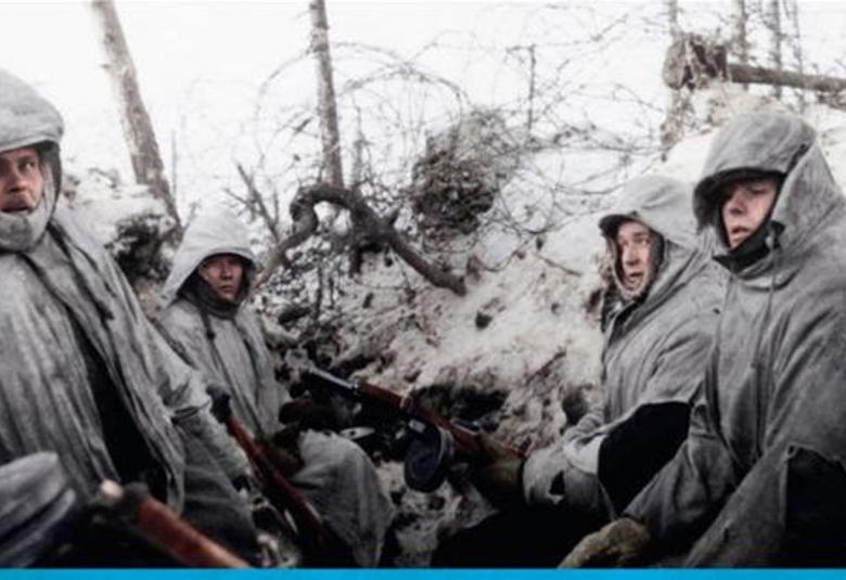 Kuvassa on sotilaita harmaatuneissa lumipuvuissa huput päässään juoksuhaudan laidalla harmaantuneessa lumessa takanaan piikkilankoja. Kuva on osa kirjankannesta.
