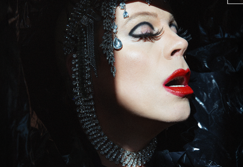 Kuvassa on Christal Snow kasvokuvassa ja kasvot ovat vinottain. Hänellä musta verkkopäähine, jossa on muutama helmikoru koristeena ja vahvaa punaista huulipunaa. Tausta on musta.