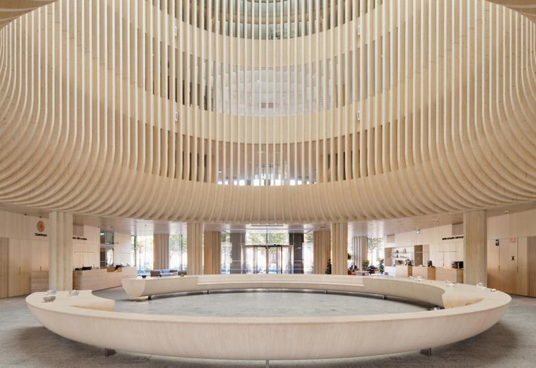 Kuvassa on yläosassa rimoista taivutettua vaaleata puuta  pyöreämuotoista rakennelmaa. Alla on pyöreä maljamainen istuin penkki.