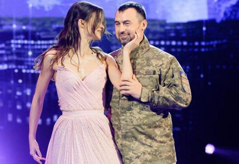Kuvassa ovat Polina Ichenko roosassa avonaisessa tanssimekossa ja Artem Moroz armeijan takissa. Taustalla on violetti kaupunkimaisema kulissi.