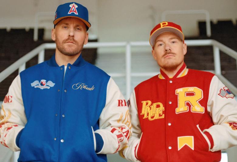 Kuvassa ovat JVG:n Jare vasemmalla sinisessä pusakassa ja oikealla VilleGalle punaisessa pusakassa seisomassa kädet taskuissa ja vastaavan väriset lippikset päässään.   Taustalla on valkoista kaidetta.