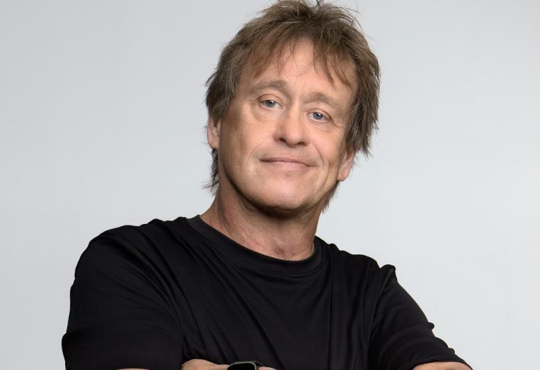 Kuvassa on Martti Syrjä ja hänellä on musta t-paita. Tausta on vaalean harmaa.