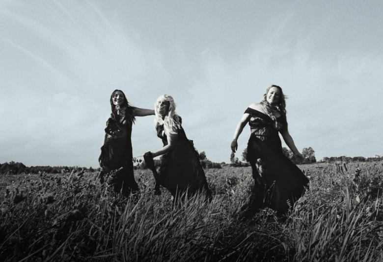 Kuvassa ovat keskellä Rodeon kolme jäsentä heinäpellossa pitkissä mekoissa seisomassa. Kuva on musta-valkoinen.