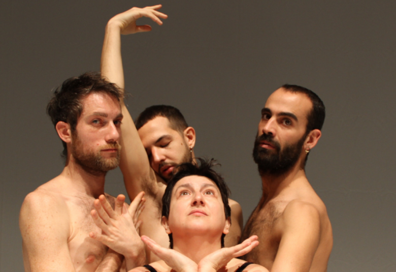 Kuvassa on viisi miestanssijaa tiiviinä ryhmänä ja kahdella heistä on yläruumis paljaana. Takana oleva ojentaa oikeaa kättään.