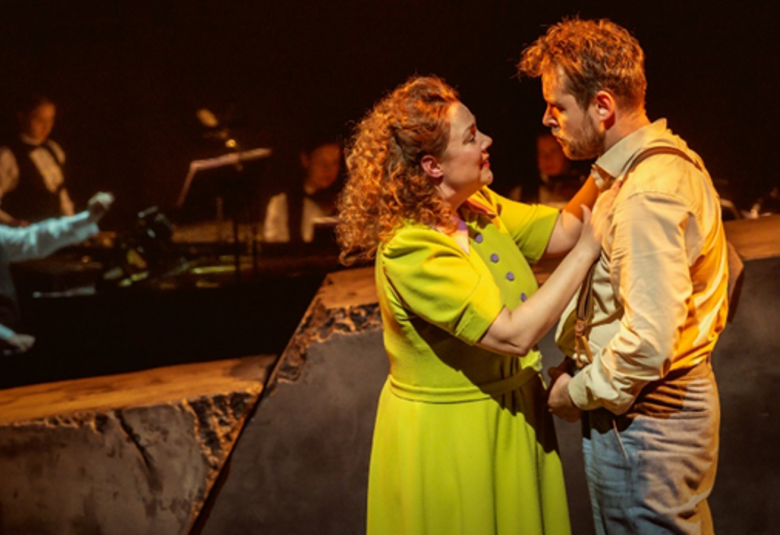 Kuvassa ovat etualalla seisomassa vasemmalla vaalean vihreässä mekossa Pihla Penttinen, joka pitää käsiään Waltteri Torikan rinnalla. Hänellä on vaalean ruskea pusero ja harmaat housut. Taustalla on himmeästi orkesteri tummalla taustalla.