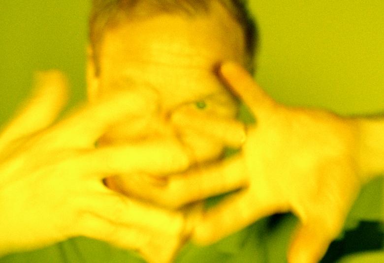 Kuvassa on Ismo Alangon kasvot ja ne ovat edessä olevien käsien takana. Sormet on haristettu. Kuvan sävy on vihertävä.