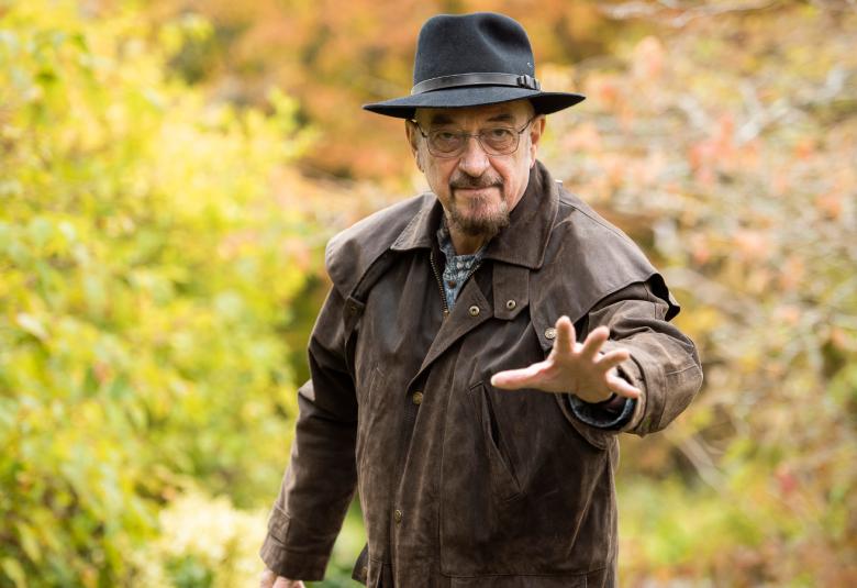 Kuvassa on Jethro Tull seisomassa ruskeassa nahkatakissa ja hattu päässään.  Hän osoittaa vasemmalla kädellään eteenpäin. Taustalla on vihreitä pensaita.