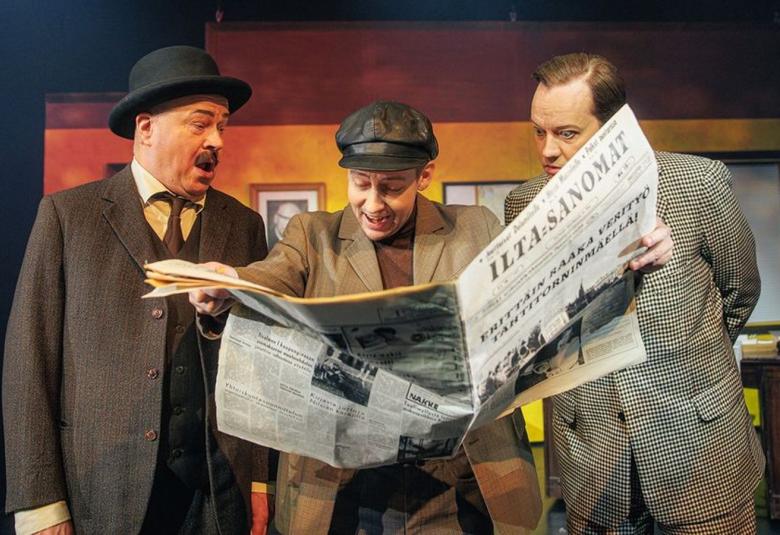 Kuvassa on seisomassa vasemmalla vanhempi mies knalli päässään ja ruskeassa takissa.  Hänen vieressään oikealla on vaalean ruskeassa takissa lukemassa Iltasanomia hämmästyneenä.  Oikealla on vaaleassa pikkuruudullisessa takissa oleva mies katsoo myös lehteä.