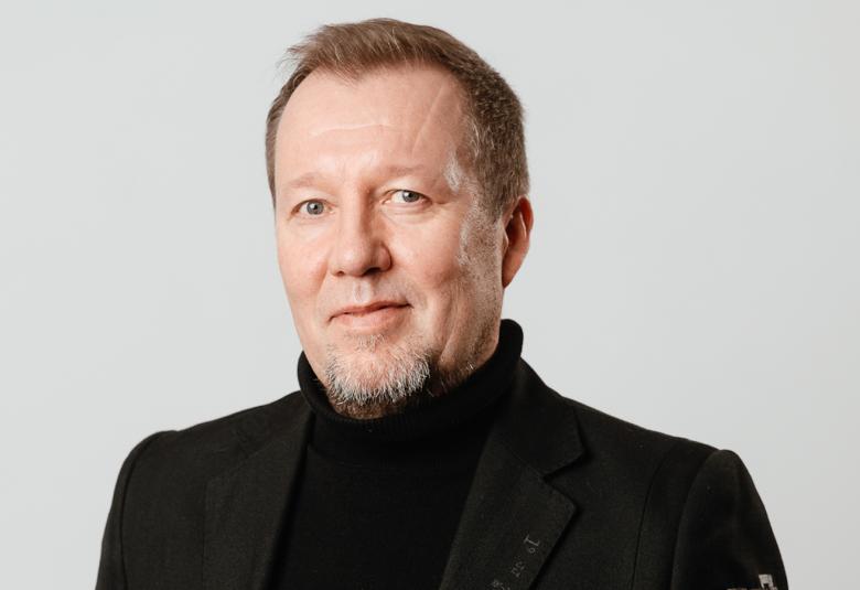 Kuvassa on Mikko Korsulainen kasvokuvassa. Hänellä on musta korkeakauluksinen paika päällään. 