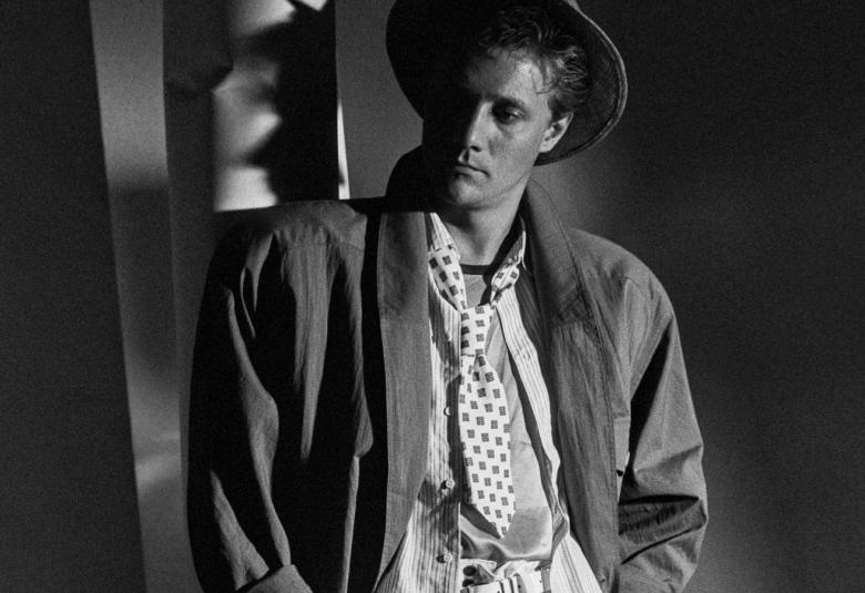 Kuvassa on nuori mies lierihatussa ja väljässä takissa ja paidassa. Kuva on musta-valkoinen.