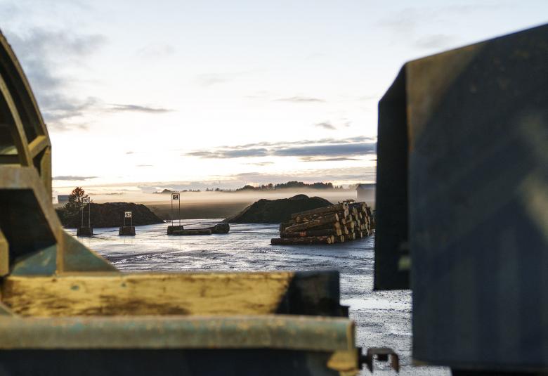 Kuvassa on vasemmalla kellertäviä mrtallirakenteita.  Edessä on vettä ja kauempanapuupino.  Oikealla on tumma, iso  metallinen seinämä.