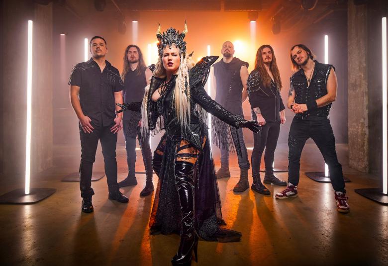 Kuvassa on edessä yhtyeen naissolisti mustassa puvussa, jossa on siipimäiset olkapäät ja päässä kruunu. Taustalla on viisi yhtyeen miesjäsentä seisomassa mustissa vaatteissa. Taustalla on pystyledvaloja ja seinien värit violettia ja oranssia.