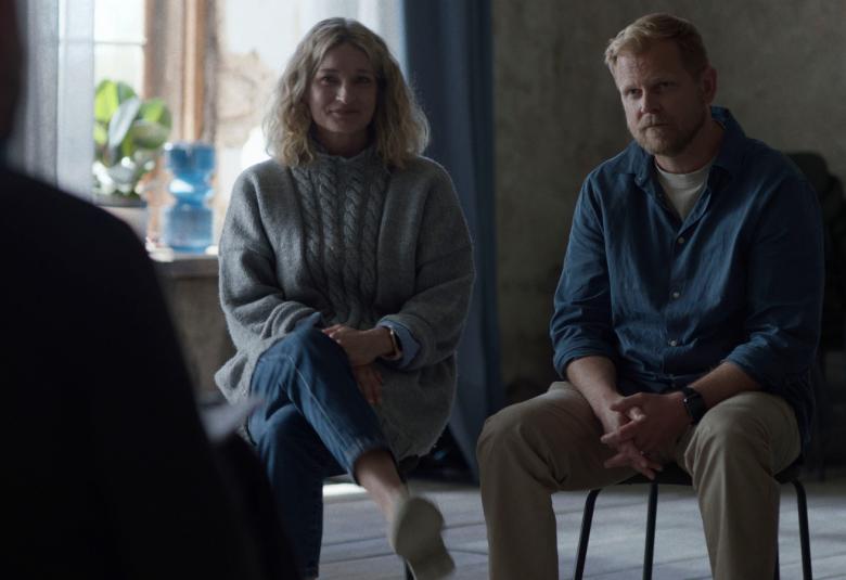 Kuvassa ovat istumassa hiukan hämärässä vasemmalla Matleena Kuusniemi ja oikealla Antti Luusuaniemi. Vasemmalla nurkassa on tumma selkä selin. Taustalla on ikkuna.