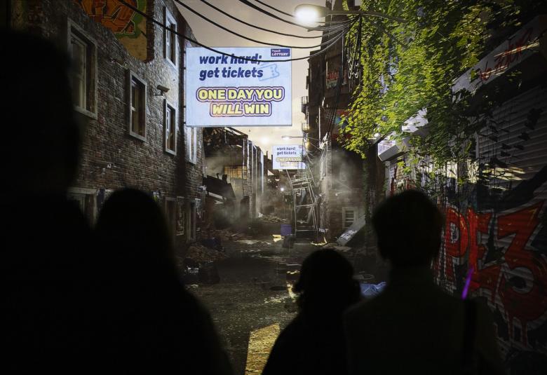 Kuvassa on tuma katunäkymä ja siinä savua ja rikkonaisia telineitä sekä kyltti, jossa lukee One day you will win.   