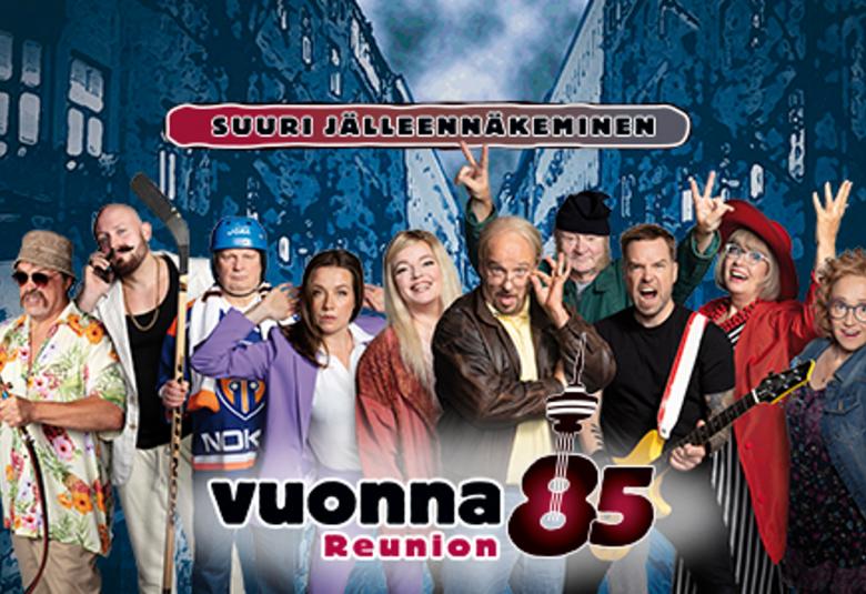 Kuvassa on yksitoista näyttelijää rivissä kesävaatteita. Yläpuolella on kyltti Suuri jälleenrakennus. Taustalla on tumman sinisiä rakennuksia.   