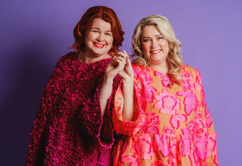 Kuvassa on vasemmalla seisomassa Ani Kellomäki viininpunaisessa mekossa  ja Tiia Koivusalo pinkissä mekossa. Tausta on lila.