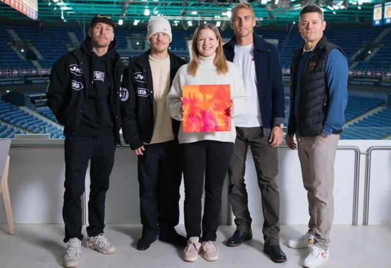 Kuvassa ovat vasemmalta VilleGalle, Jare ja Sari Aalto-Setälä kädessään oranssin pinkki levyn kansi ja Jokereiden edustajat seisomassa Jäähallissa taustallaan tyhjä katsomo.