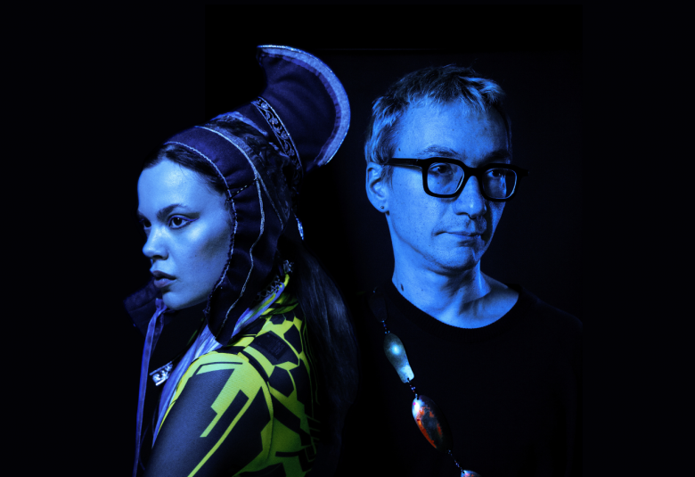 Kuvassa on puolivartalokuvassa vasemmalla Hilda Länsman sivukuvassa ja hänellä on Lapin puvun päähine ja puku. Oikealla on Tuomas Norvio mustassa t-paidassa. Kuvan sävy on tumma.