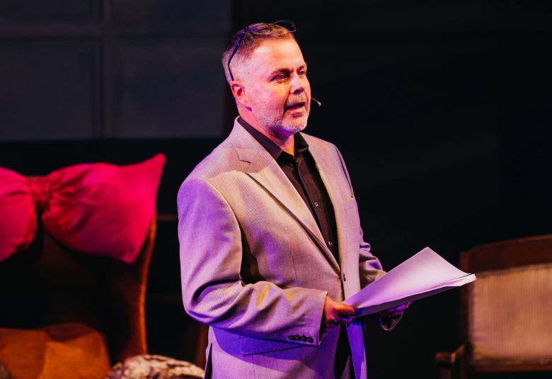 Kuvassa on keskellä Pekka Laasonen seisomassa teatterin penkkien välissä ja seisoo sivuttain. Hänellä on vaalea takki päällään ja käsikirjoitus kädessään. Tausta on tumma.