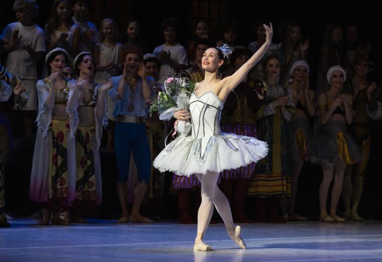 Kuvassa on keskellä valkoisessa balettipuvussa Sofia Gustafsson ja hänellä on vasen käsi ojennettuna sekä kukat oikeassa kädessään. Taustalla näkyy himmeästi muita esiintyjiä.