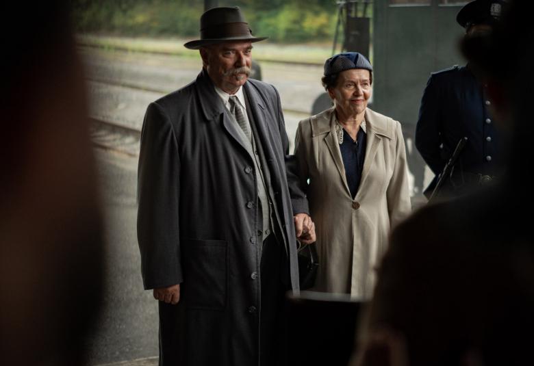 Kuvassa ovat vasemmalla Pertti Sveholm harmaassa takissa. Hänen vieressään oikealla on ruskehtava takki päällään. Mustaa on kuvan molemmissa reunoissa.