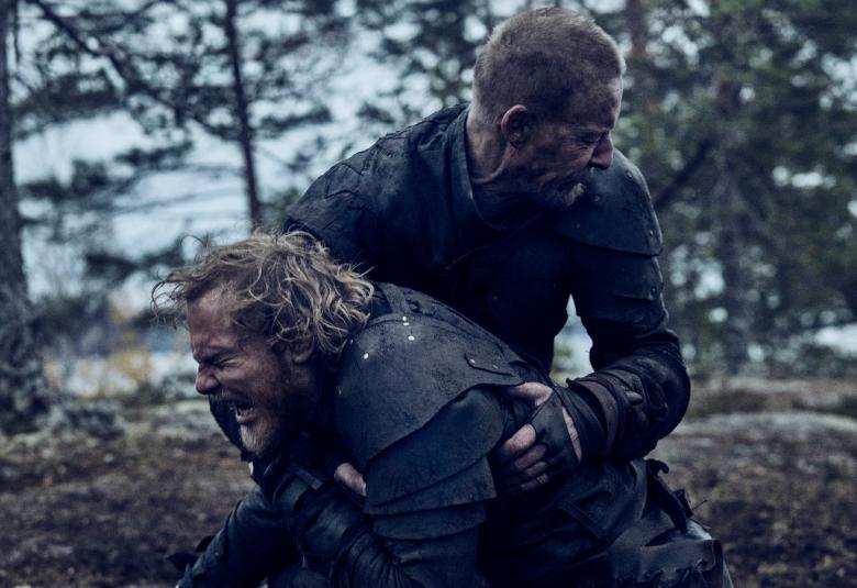 Kuvassa ovat Elias Salonen edessä ja häntä pitää syliotteessa Eero Aho. Taustalla on mäntymetsää.