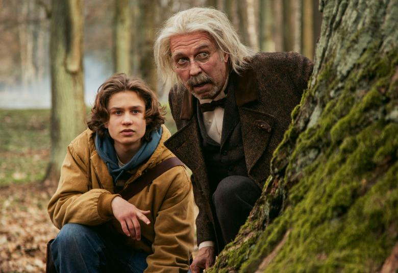 Kuvassa ovat vasemmalla metsässä kyykyssä suuren puunrungon vieressä Kuura Rossi ja hänen vieressään vähän ylempänä Martti suosalo pitkissä vaaleissa hiuksissa. Taustalla näkyy puunrunkoja.