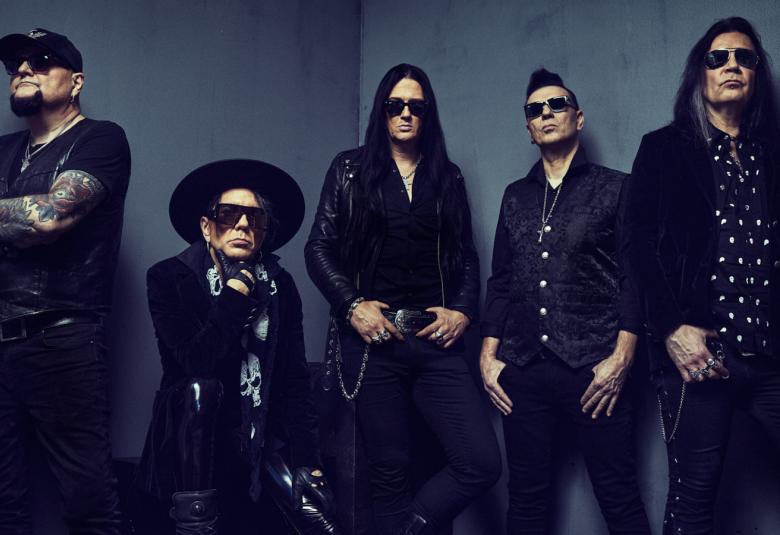 Kuvassa on tumman harmaalla pohjalla The 69 eyes -bändin viisi miestä mustissa vaatteissa, joista neljä seisoo ja yksi istuu. 