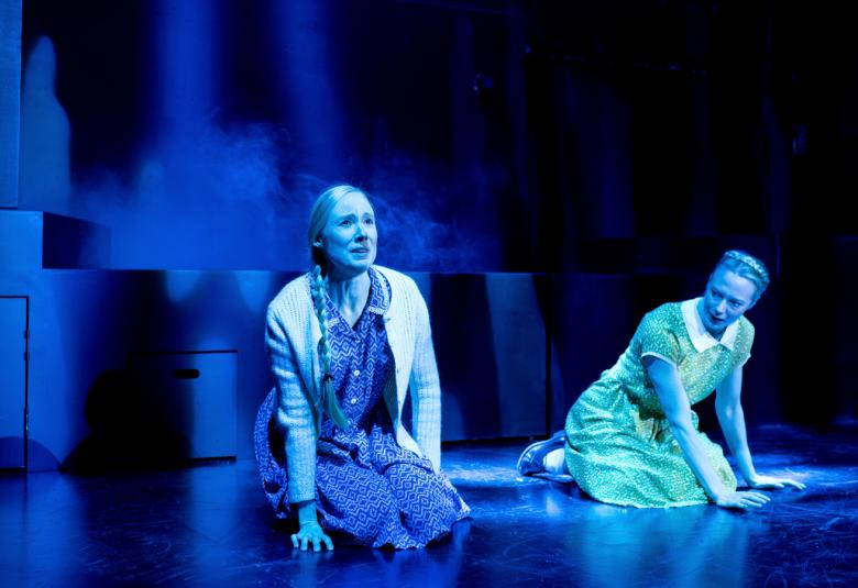 Kuvassa ovat Inka Reyes ja Heidi Ajanto polvillaan näyttämöllä. Kuvan sävy on sininen.