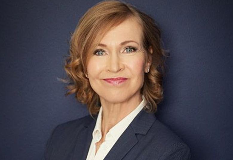 Kuvassa on Leena Niemistö ja hän on puolivartalokuvassa. Hänellä on tumman sininen jakku ja valkoinen paitapusero päällään sekä puolipitkät, kiharat punertavat hiukseton. Tausta on tumman sininen. 