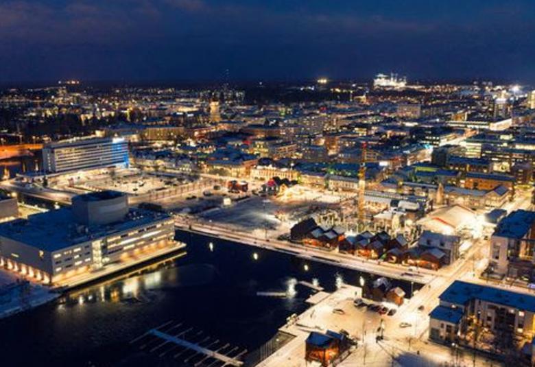 Kuvassa on ylhäältä päin kuvattuna Oulun keskustaa illalla ja se on valaistu. 