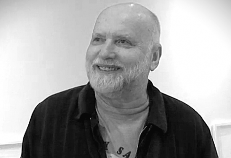 Kuvassa on Arvo Siikamäki ja hän on puolivartalokuvassa. Hänellä on tumma pusero ja vaaleahko t-paita päällään.  Hänellä on vaaleaa partaa ja päälaki on hiukseton. Kuva on musta-valkoinen.