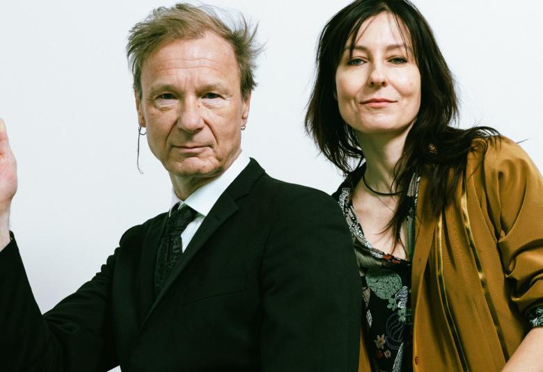 Kuvassa on vasemmalla Ismo Alanko puolivartalokuvassa mustassa takissa. Hänellä on oikea käsi nostettuna sivulle. Oikealla on Mariska ruskeassa villa takissa ja harmaassa puserossa.