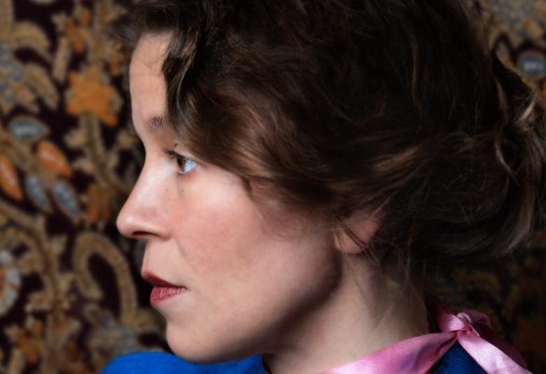 Kuvassa on Viivi Prokofjev sivukuvassa. Hänellä on surkeat kiharat hiukset. Taustalla on ruskean kirjavaa tapettia.