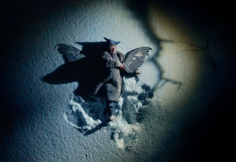 Kuvassa on mies makaamassa hangellaja hänellä on vaakasuikkahattu päässää sekä peitto päällään. Hänen vieressään näkyy tummia siipiä. Kuvaan tulee keskelle valoa ja reunat ovat tummat.