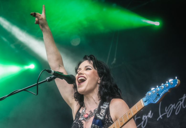 Kuvassa on Erja Lyytinen kuvattuna alaviistosta ylöspäin ja hän on laulamassa mikki edessään. Hänellä on oikea käsi pystyssä ja päällään hihaton pusero sekä kitara kädessään. Taustalta tulee vihreää valoa.