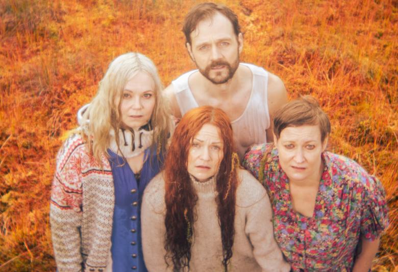 Kuvassa on ylhäältä päin kuvattuna edessä kolme naisnäyttelijää ja takana yksi mies. He ovat tiiviinä ryhmänä. Tausta on oranssi.