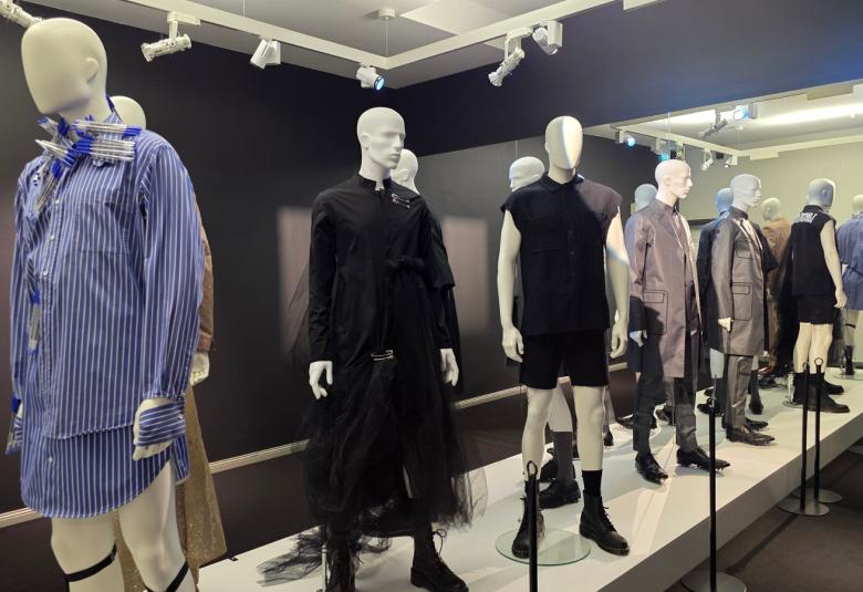 Kuvassa on miesmallinukkeja ja vasemmalla on sinipaitainen mallinukke.  Muut ovat rivissä mustissa ja ruskehtavissa väreissä. 