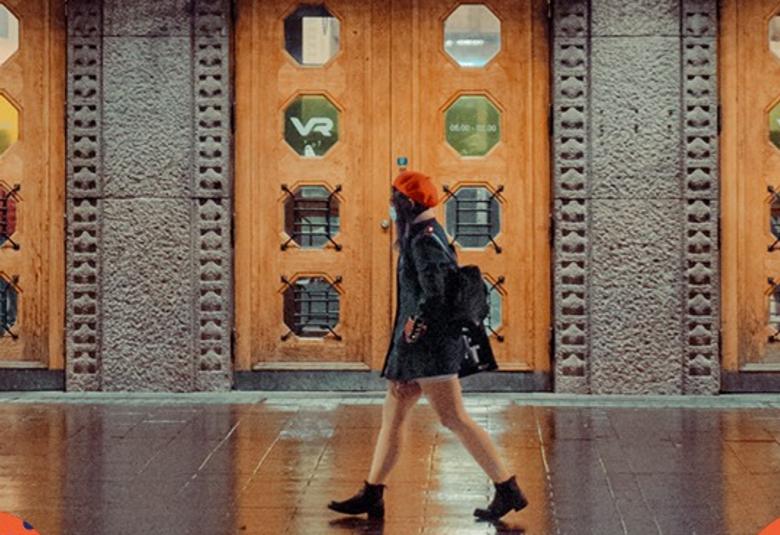 Kuvassa on Helsingin rautatieaseman pääovia, jotka ovat ruskeaa puuta ja niissä on kahdeksan pyöreää lasia. välissä on harmaata graniittia ja niissä koristeelliset reunukset. Keskellä kävelee nuori nainen mustassa takissa ja punaisessa baskerissa.