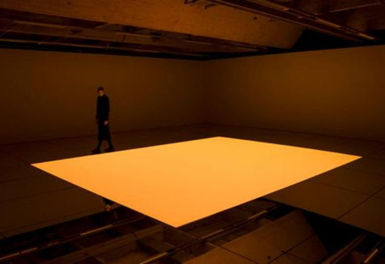 Kuvassa on ruskeassa tilassa kelluva, hiukan kaareva neliömäinen oranssi laatta.