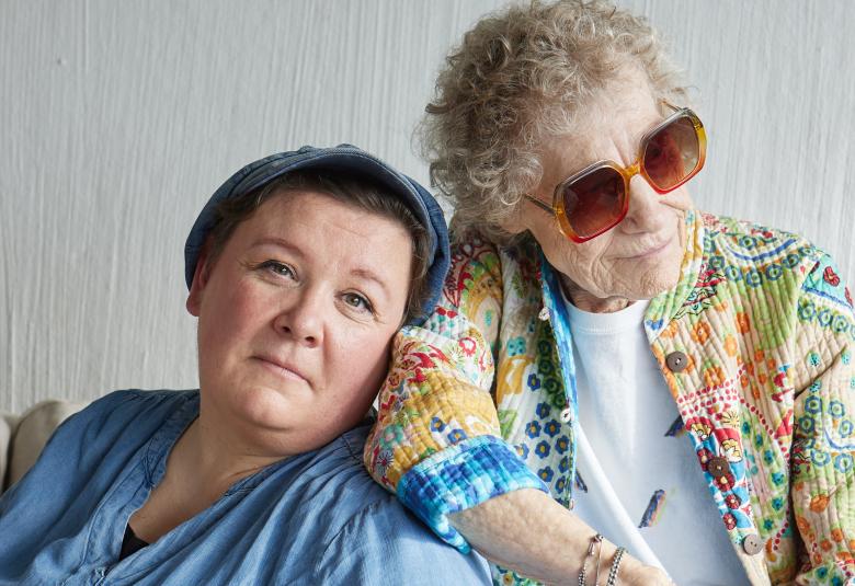 Kuvassa ovat vasemmalla puolivartalokuvassa istumassa vasemmalla Maija Kaunismaa vaalean sinisessä puserossa. Hän nojaa Chrisse Johanssoniin, jolla on aurinkolasit ja turkoosin ja vaalean ruskean kuvioinen pusero päällään. Tausta on vaalea.