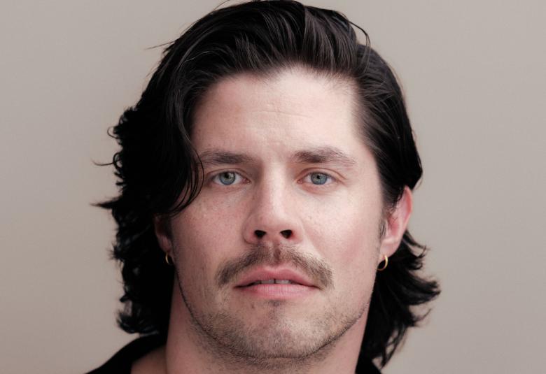 Kuvassa on Markku Haussilan kasvokuva ja hänellä on tummat puolipitkät hiukset. Tausta on harmaa.