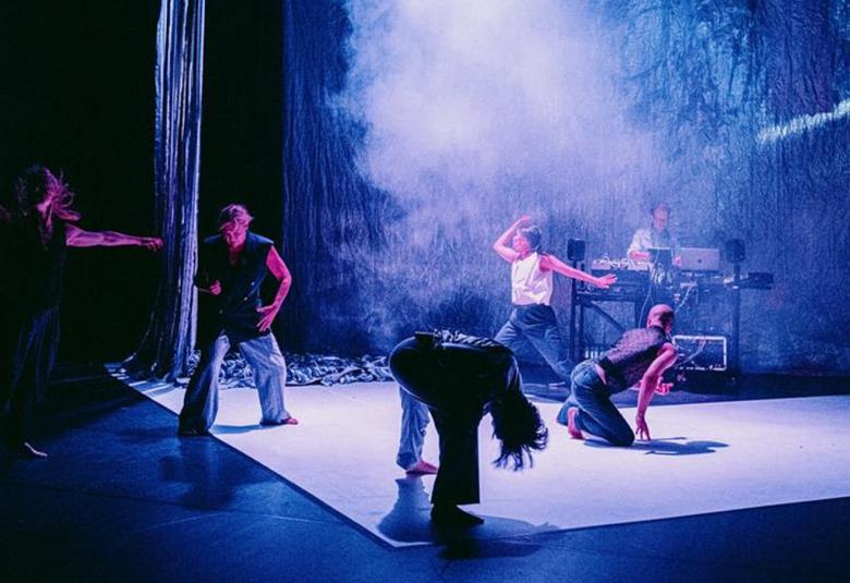 Kuvassa on sinisellä valolla valaistulla näyttämöllä neljä tanssijaa erilaisissa asennoissa. Heillä  on farkkuhouut ja eerilaisia paitoja. Keskellä on vaaleaa savua.