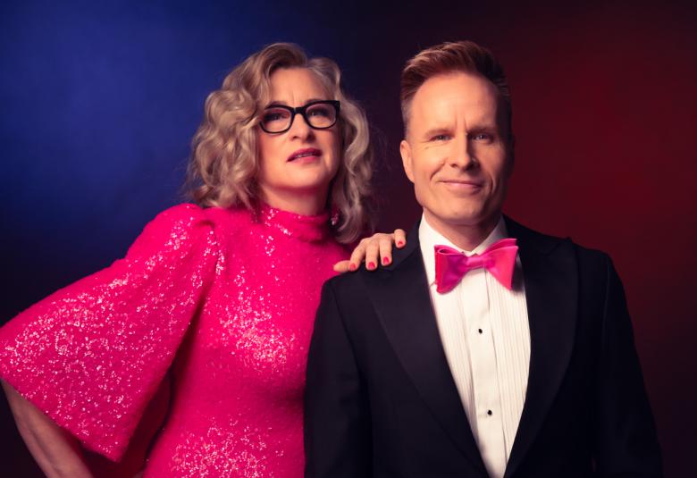 Kuvassa on vasemmalla Katja Ståhl pinkissä, glittermekossa, jossa on leveä hihat. Hän pitää vasenta kättään Mikko Kekäläisen olkapäällä, jolla on musta takki, valkoinen paita ja pinkki rusetti. He ovat puolivartalokuvassa. Tausta on tummansininen.