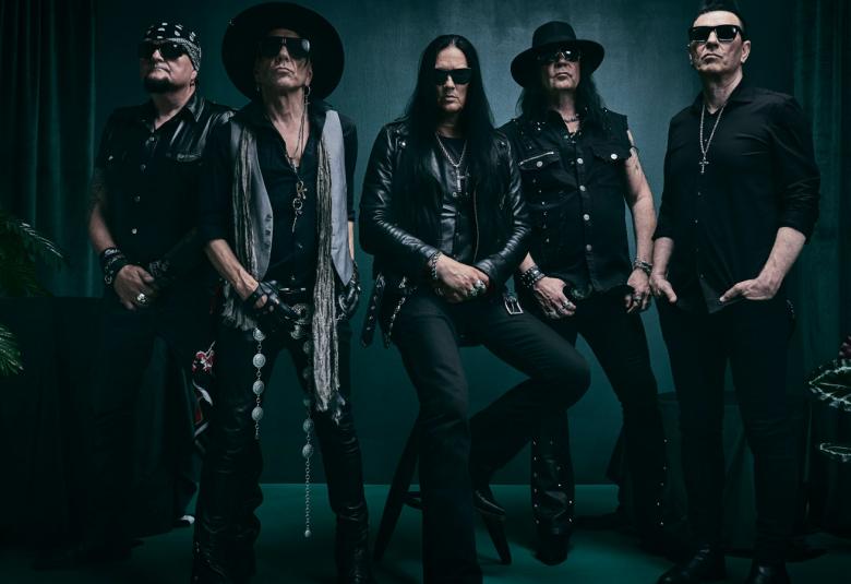 Kuvassa on viisi yhtyeen jäsentä seisomassa ja heillä on mustat vaatteet päällään. Kuvan sävy on tumma.