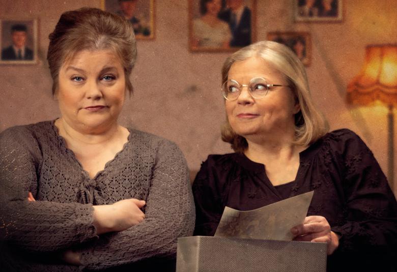 Kuvassa on vasemmalla nainen ruskeassa villapuserossa kädet puuskassa. Oikealla on nainen mustassa puserossa ja hän katsoo vasemmalla olevaa. Taustalla on huonetta.